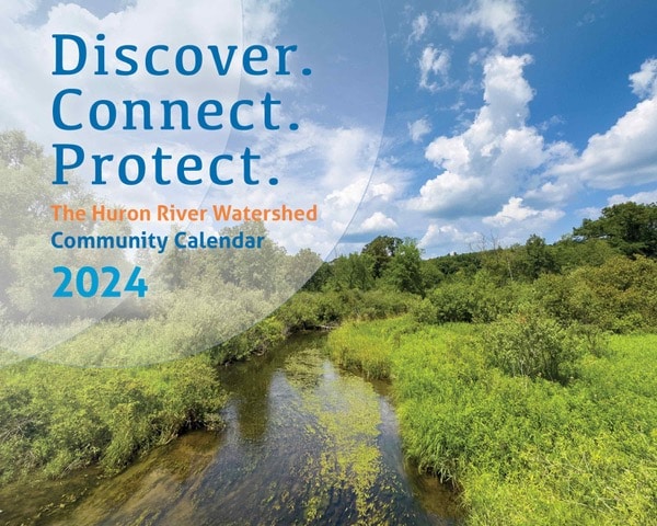 A picture of the cover of the 2024 Huron River Watershed Community Calendar containing a photo of a creek with blue sky and trees.
